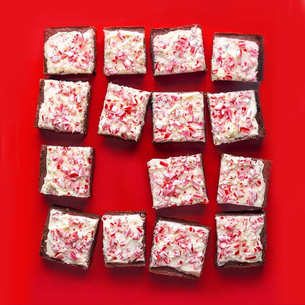 Fifteen brownies, frosted with white frosting and speckled with crushed peppermint candies.