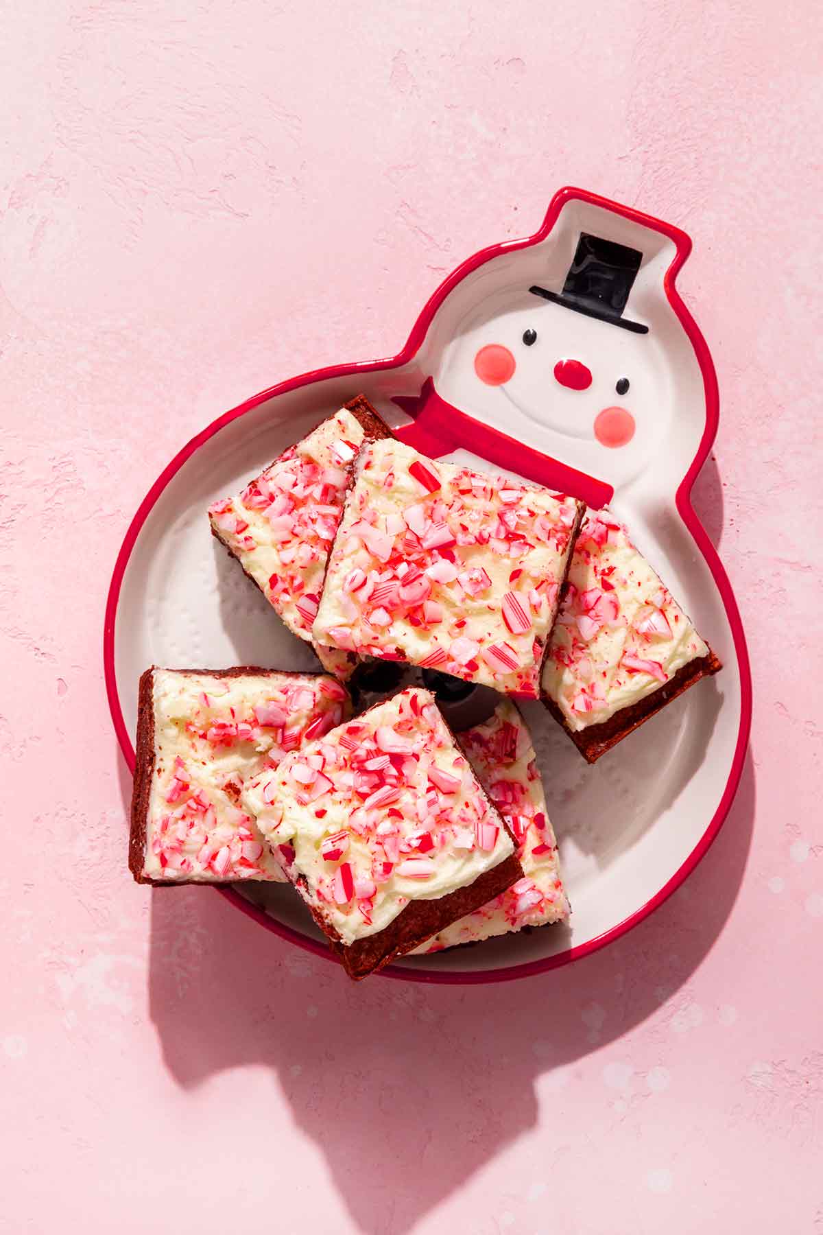 A snowman dish filled with 6 peppermint brownies on a pink background.