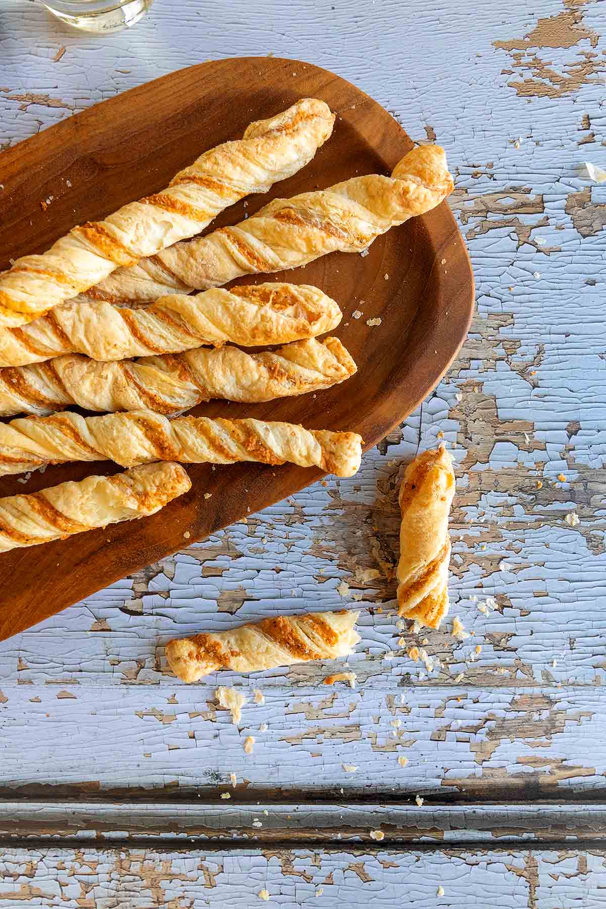 Cheese straws on an oval wooden platter on a distressed wooden surface.