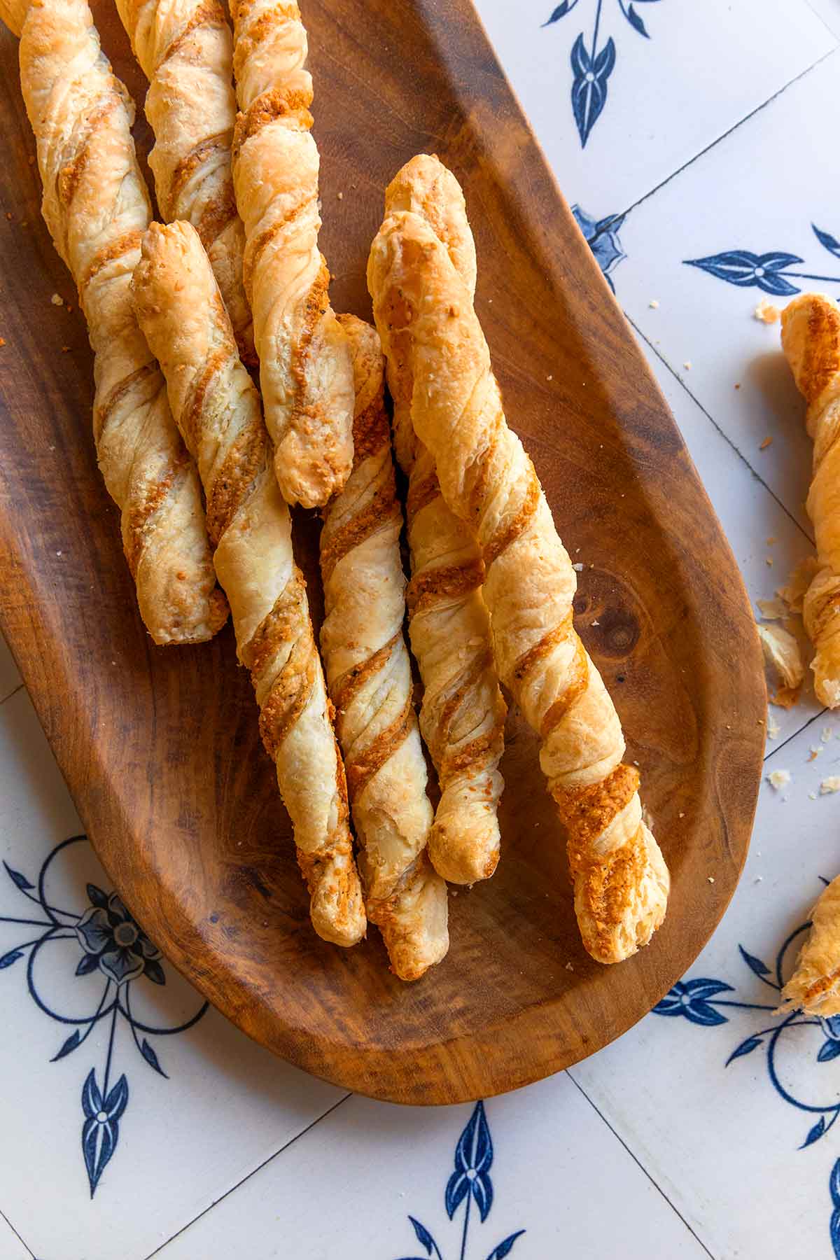 Cheese straws on a wooden oval platter on a blue and white tiled background.
