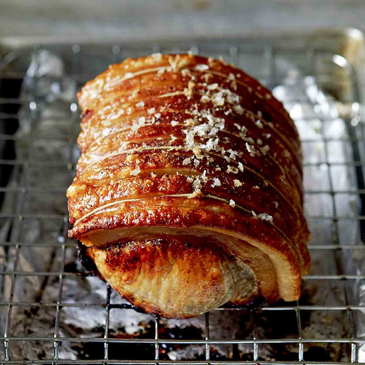 A pork loin roast, tied and seasoned with salt and pepper, on a foil-lined sheet pan with a wire rack.