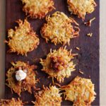 Nine potato latkes with apple-date chutney and cinnamon sour cream on a wooden cutting board.