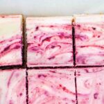 A slab of red wine cherry cheesecake bars cut into squares.