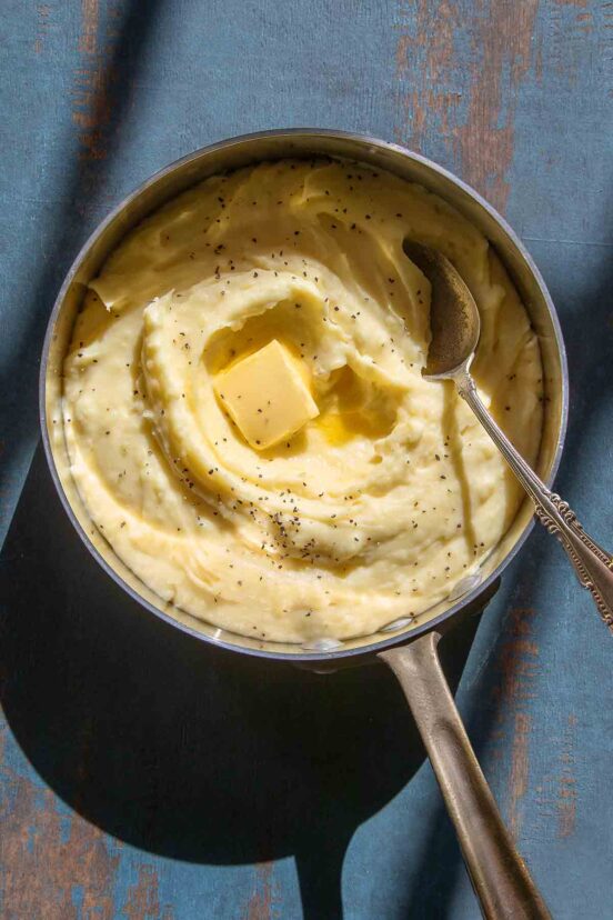 A saucepan filled with roasted garlic mashed potatoes with a pat of butter on top.