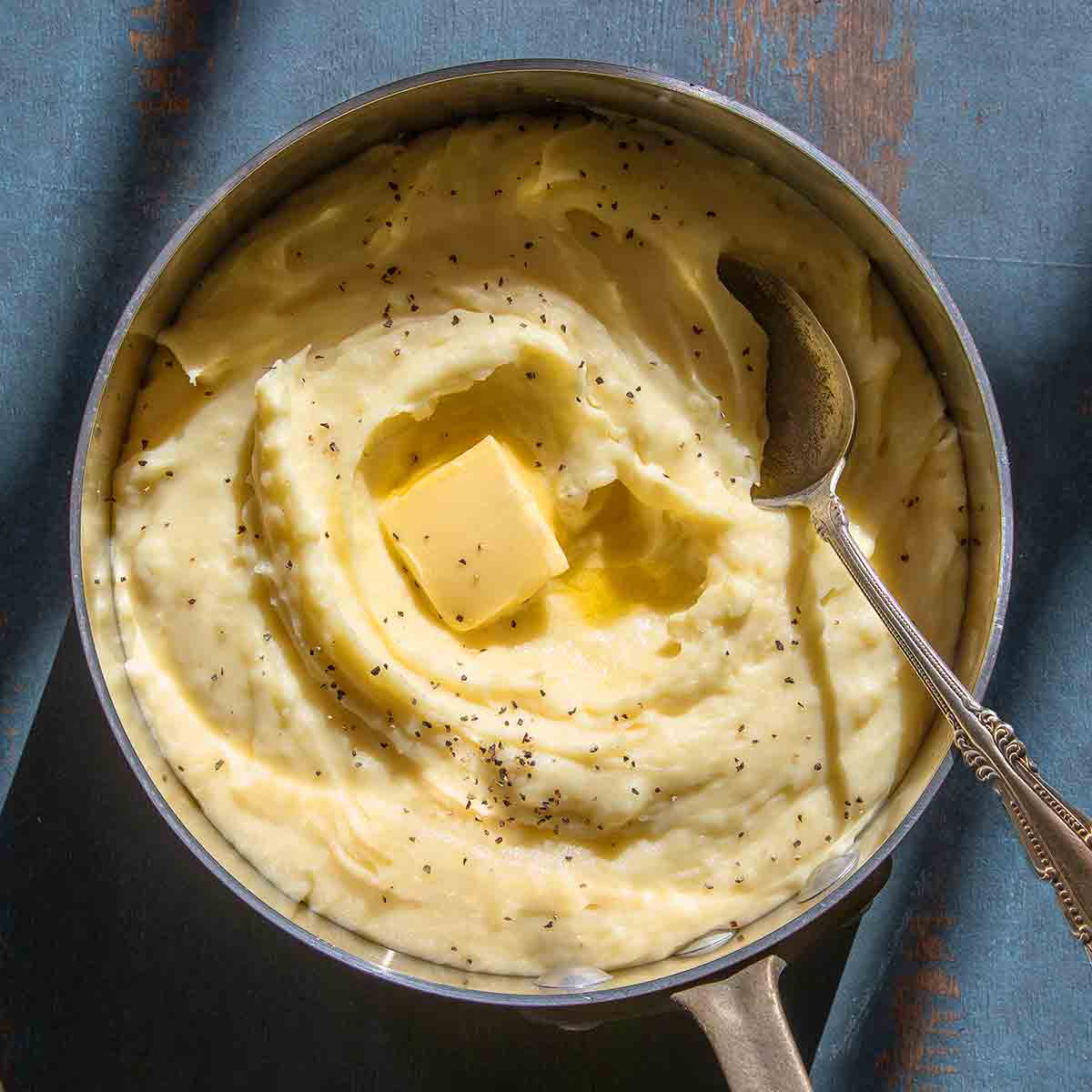 A saucepan filled with roasted garlic mashed potatoes with a pat of butter on top.