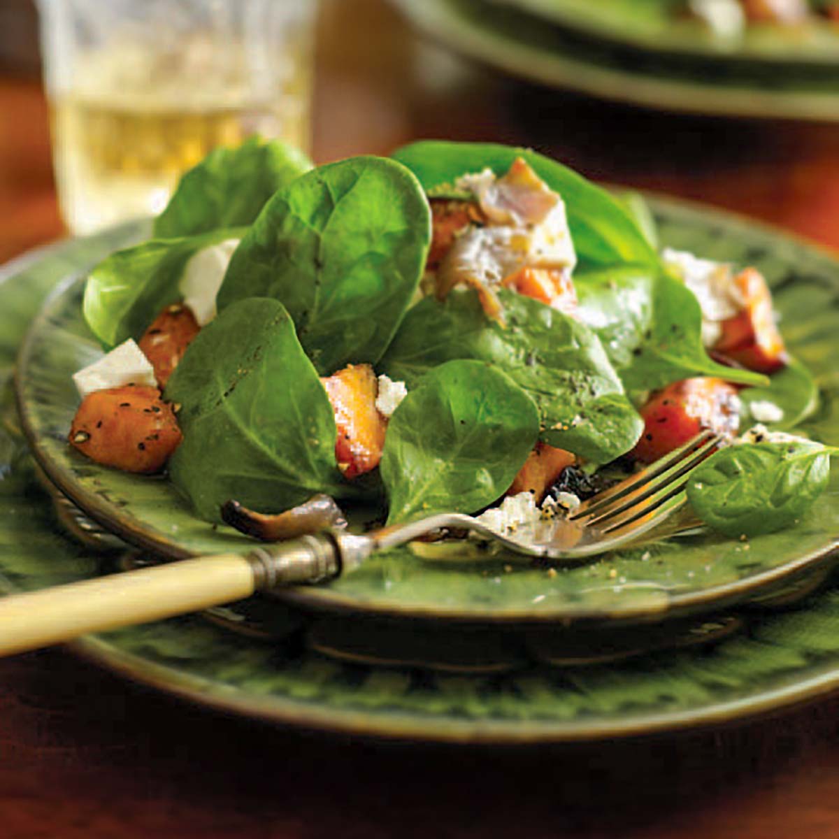 A serving of roasted sweet potato and feta salad on a green plate with a fork resting on the plate.