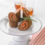 A white cake stand with four spirals of pumpernickel bread, salmon mousse, and smoked salmon.
