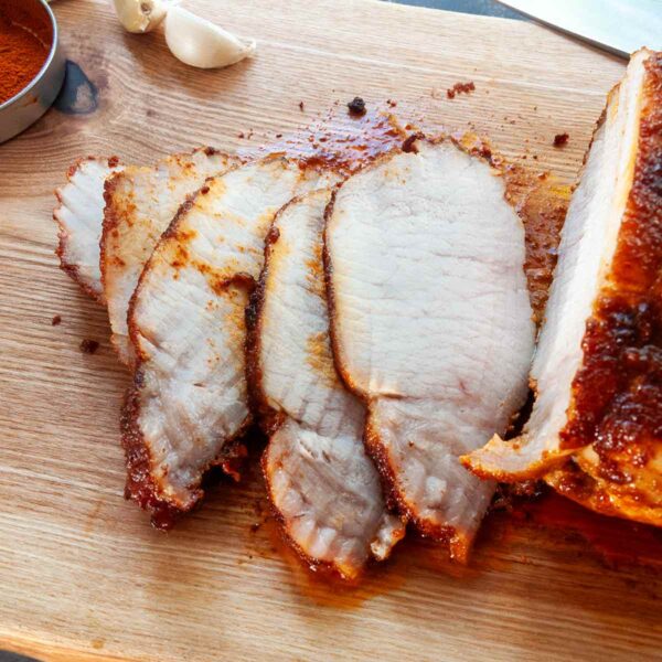 A partially sliced pork loin roast on a cutting board with garlic and paprika.