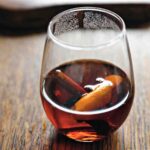 Spiced cider with a cinnamon stick and orange zest, in a stemless wine glass.