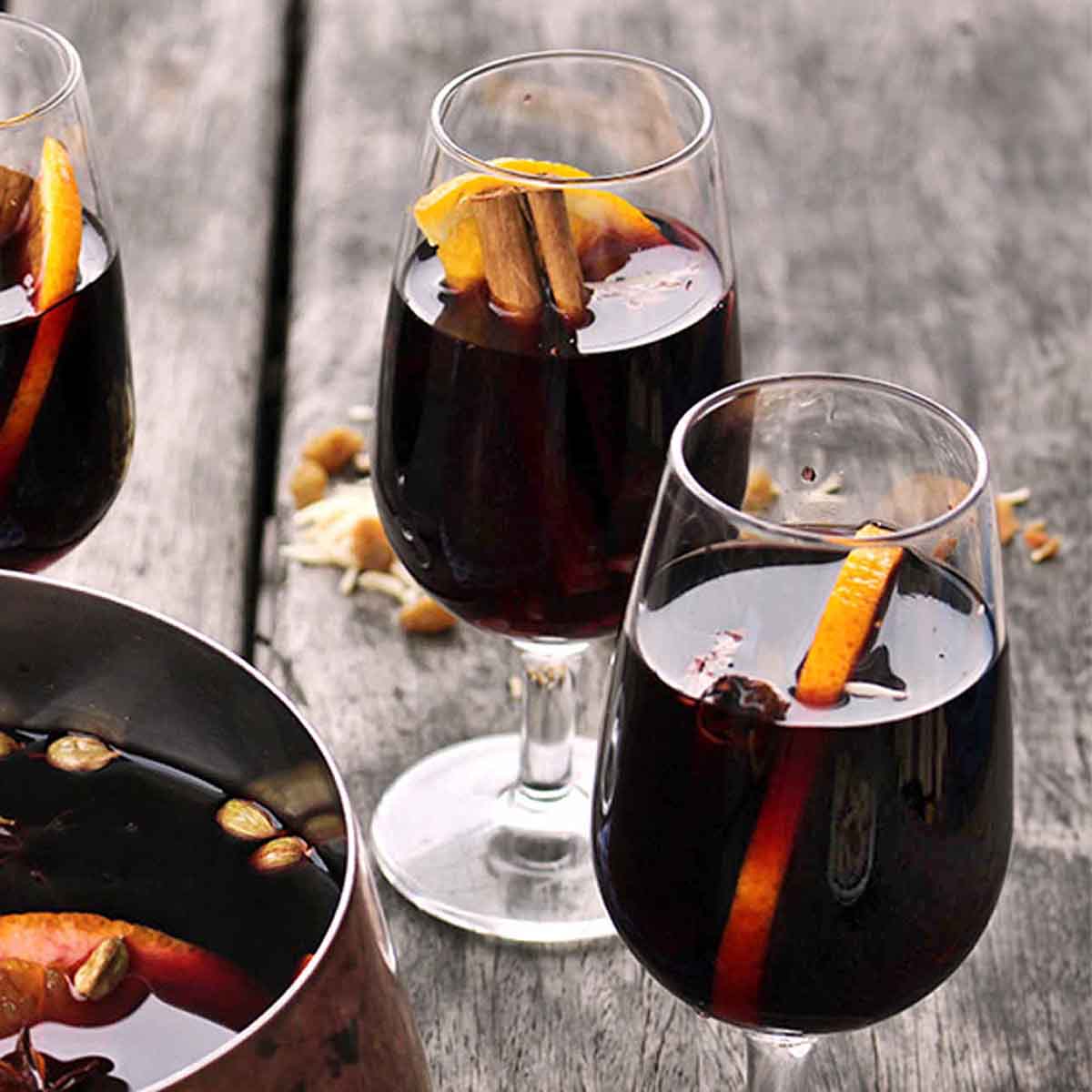 Three glasses of glogg (mulled wine) with orange slices and cinnamon sticks.