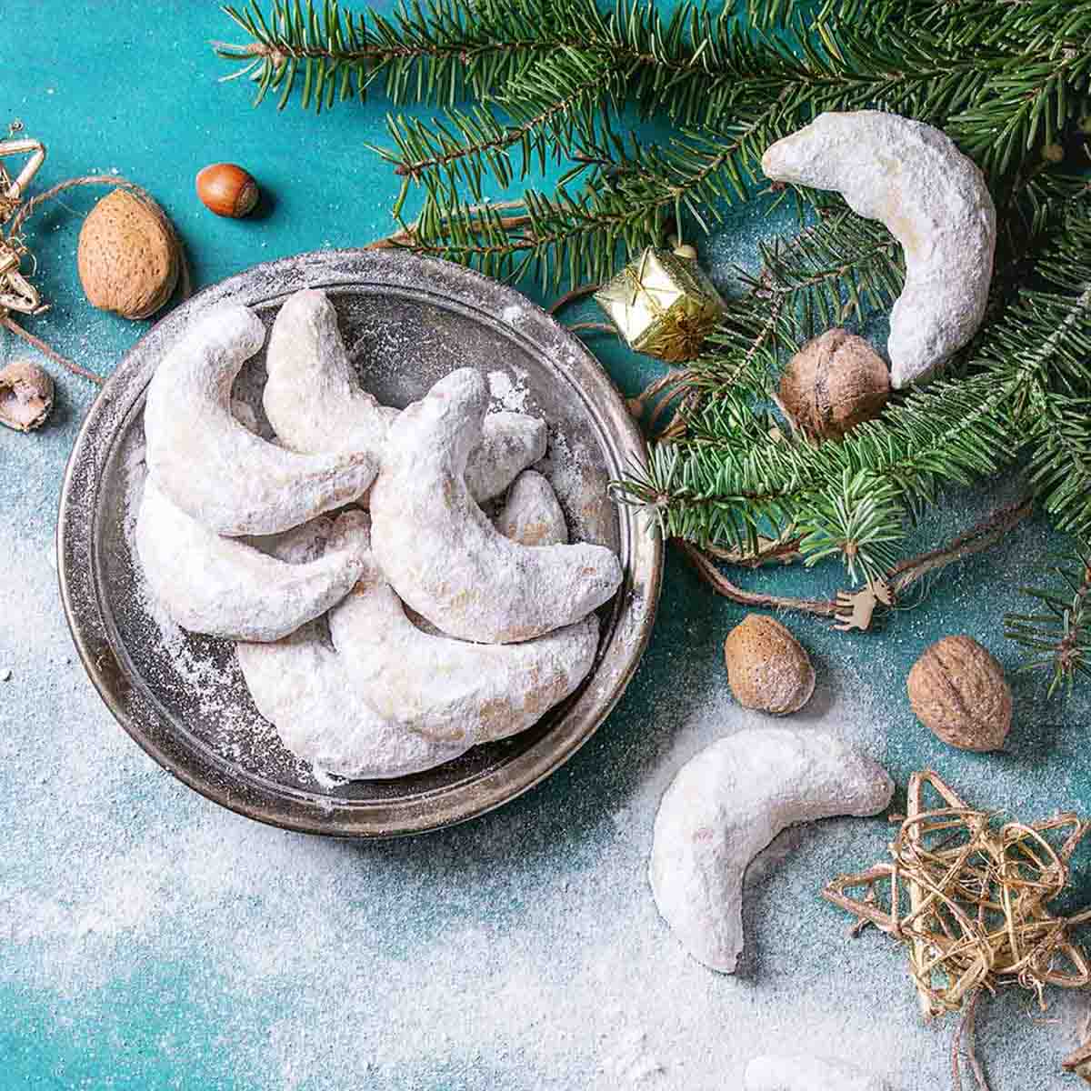 A pile of crescent-shaped cookies on a platter with greenery and Christmas ornaments on the side.