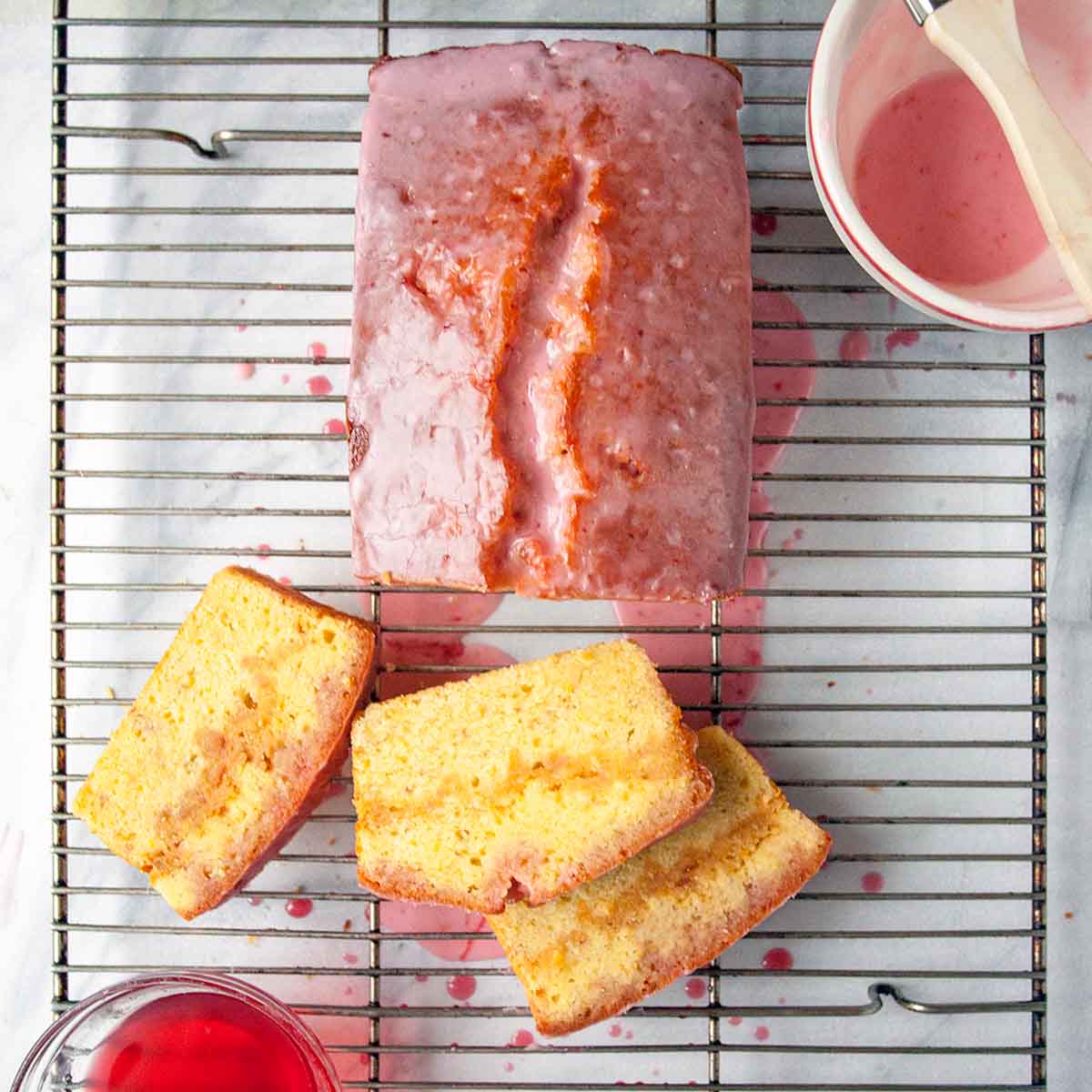 A blood orange pound cake on a wire rack with glaze and sugar syrup, three slices cut.