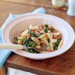 Bowl of cavatelli with turkey sausage, tomato, and broccoli rabe on a table, with a spoon.