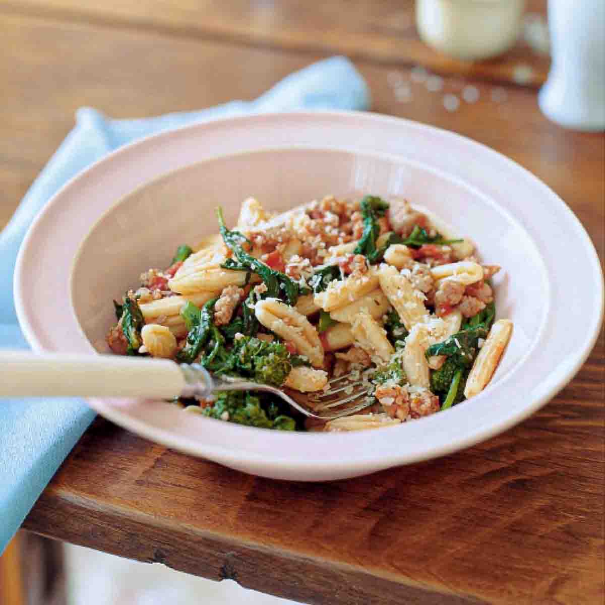 Bowl of cavatelli with turkey sausage, tomato, and broccoli rabe on a table, with a spoon.