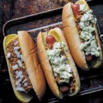One chili bun and two slaw dogs on a rimmed baking sheet.