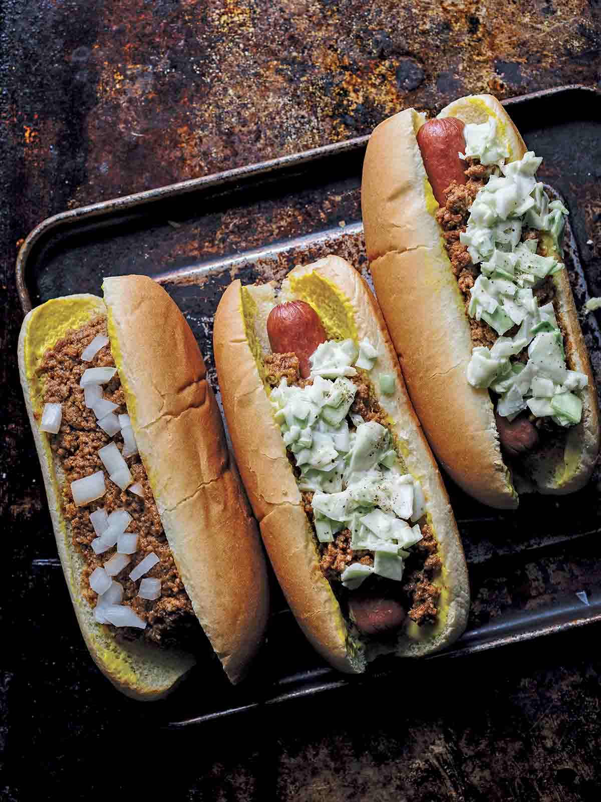 One chili bun and two slaw dogs on a rimmed baking sheet.