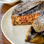 An eggplant timbale with one wedge cut from it on a white plate.
