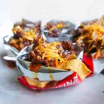 Chili and grated cheddar on top of Fritos in open mini bags of Fritos.
