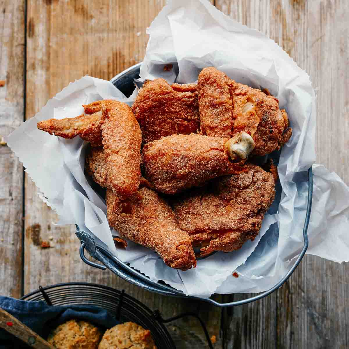 Several pieces of gluten-free dairy-free fried chicken in a parchment-lined metal bucket.