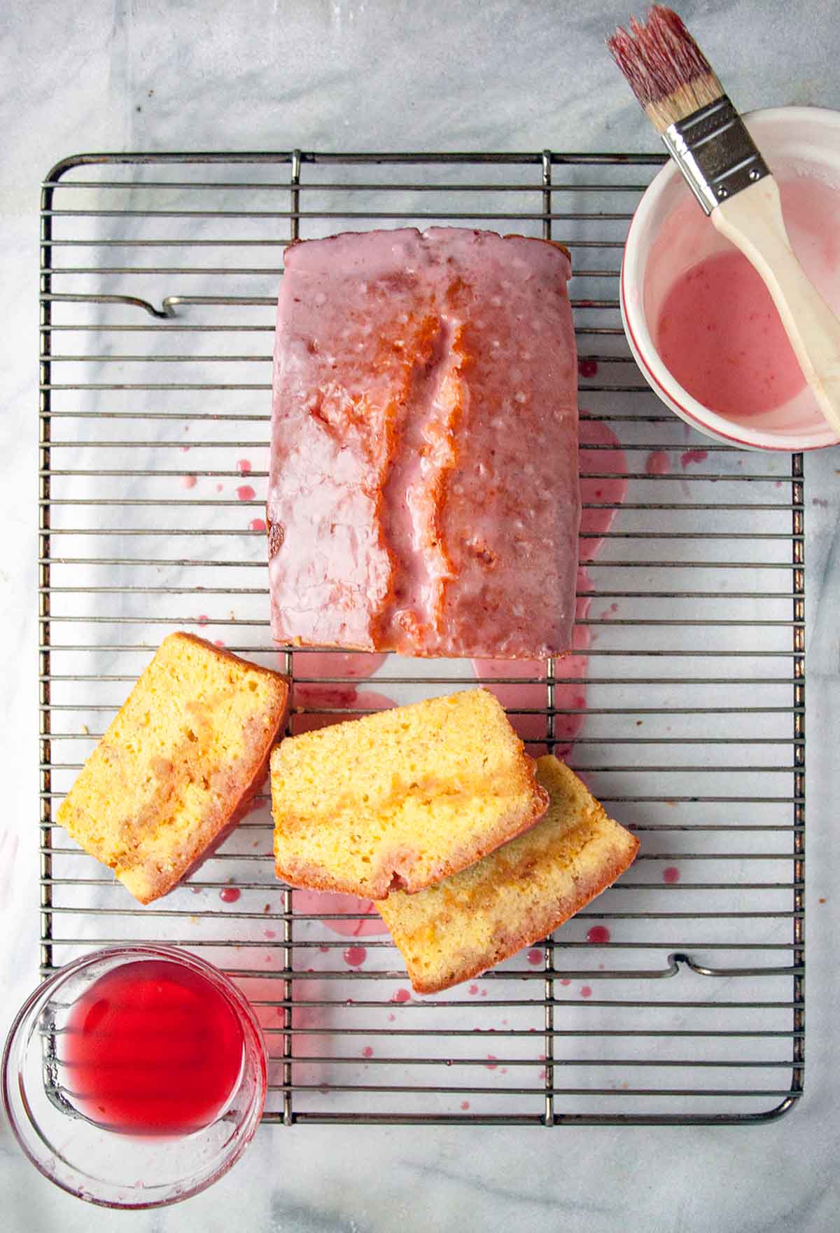 A blood orange pound cake on a wire rack with glaze and sugar syrup, three slices cut.