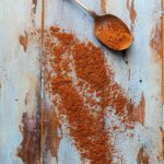 A spoonful of Shawarma spice blend on a wooden surface with some of the spice mix scattered nearby.