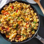 A pan of skillet tortellini with sausage and cherry tomatoes sprinkled with chopped basil.