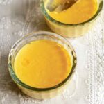 Two glass dishes of orange flan on a lace tablecloth.