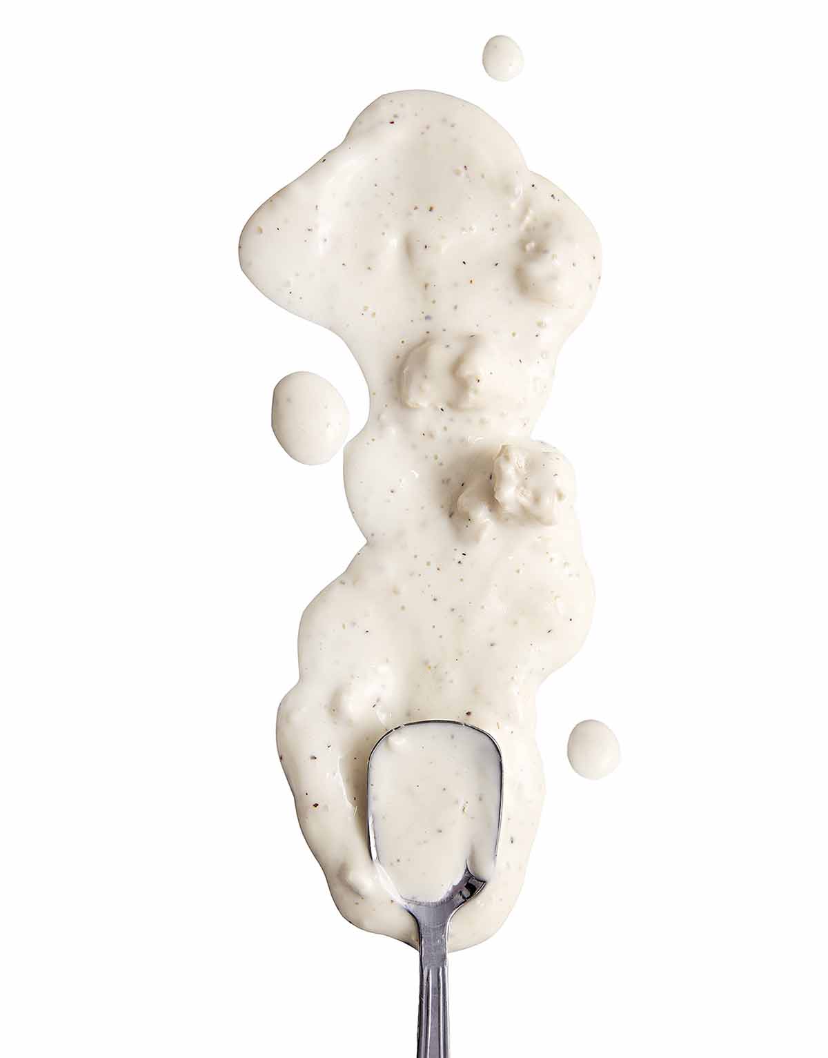 Blue cheese dip, with chunks of blue cheese, spilled in a white background with a spoon.