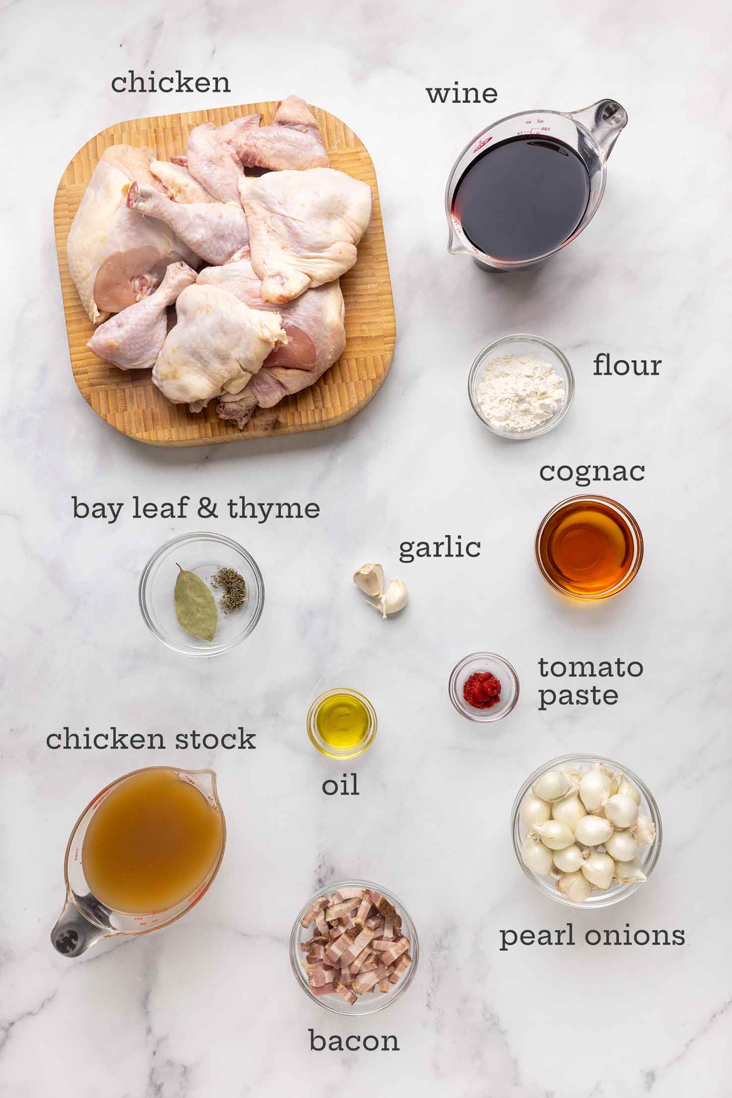 Ingredients for coq au vin--chicken, wine, flour, Cognac, bay leaf, thyme, garlic, oil, stock, tomato paste, bacon, and onions.