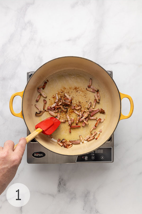 A man's hand sauteing lardons being sautéed in a Dutch oven.