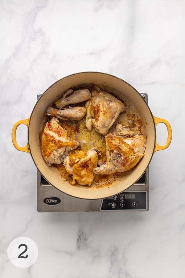 Chicken pieces browning in bacon fat in a Dutch oven.