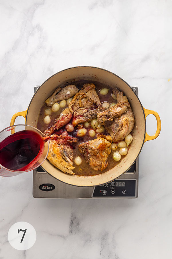 Wine being poured into a Dutch oven with chicken