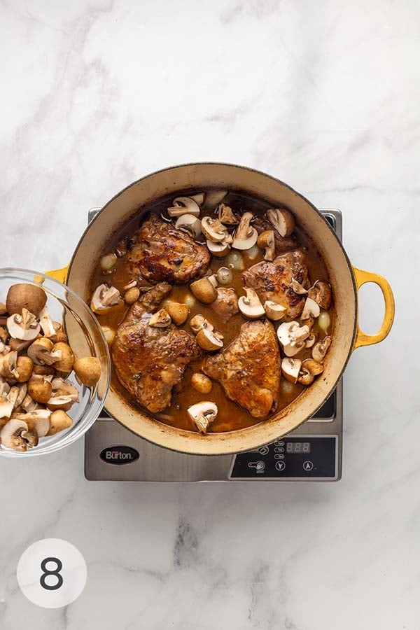 Pearl onions and mushrooms being added to a pot of coq au vin (chicken stew).