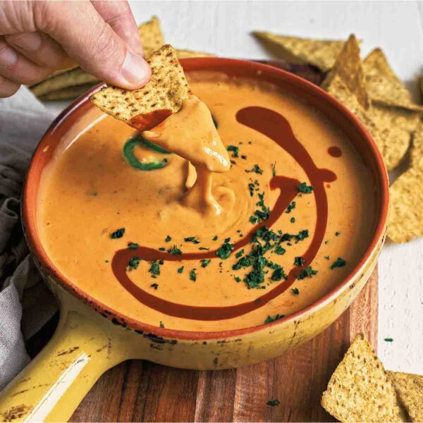 A bowl of easy queso dip with a person dipping a chip into it.
