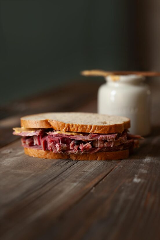 Several slices of homemade corned beef in a sandwich on a wooden table.