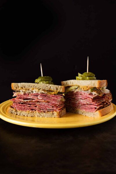 A halved pastrami sandwich on a yellow plate.