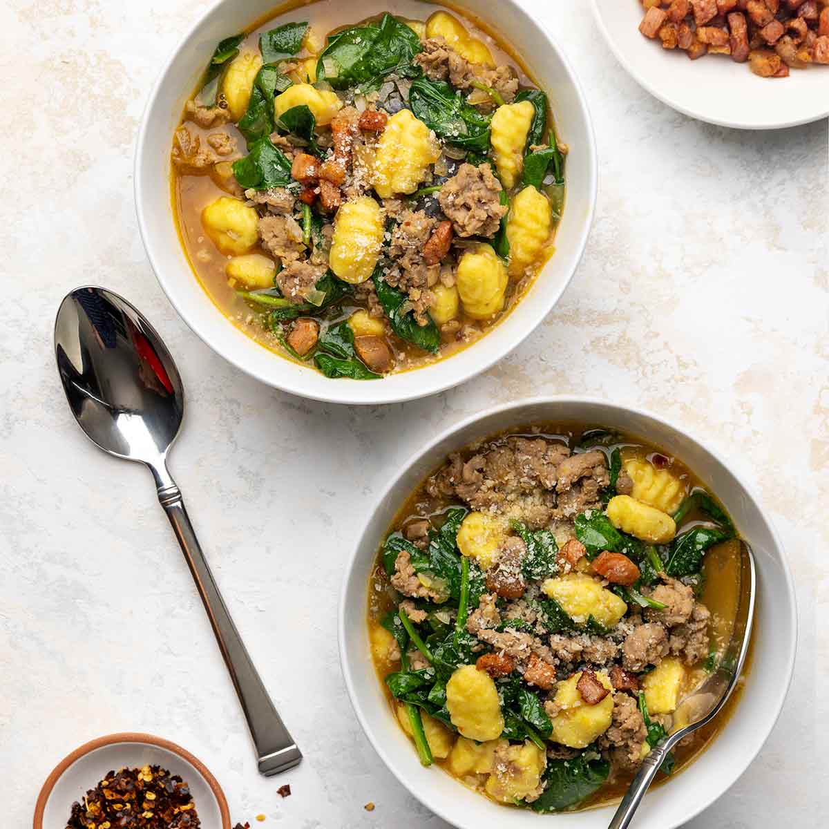 Two bowls of Italian sausage soup with gnocchi and spinach.