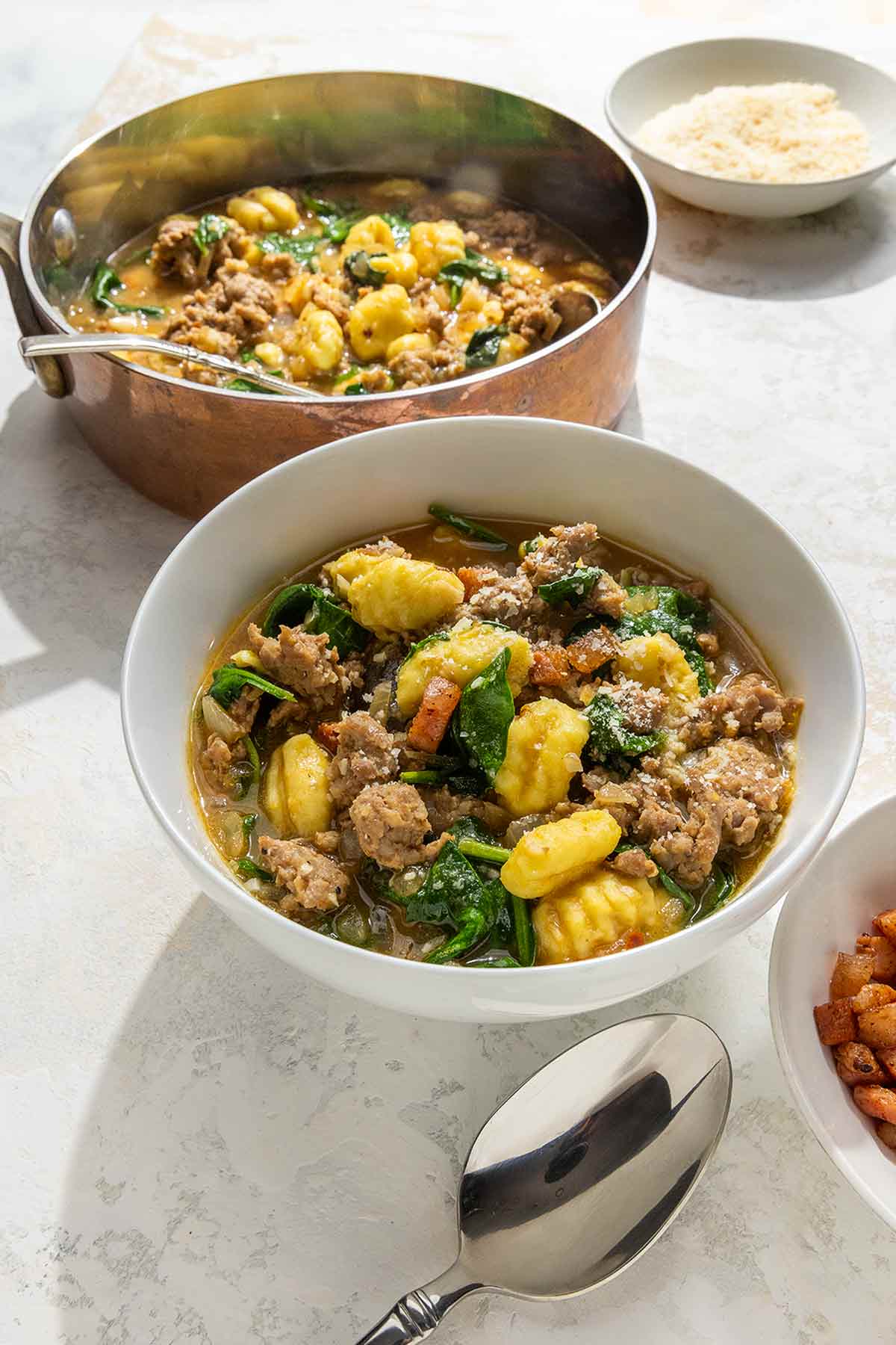 A pot and a bowl of bowl of Italian sausage soup with gnocchi.