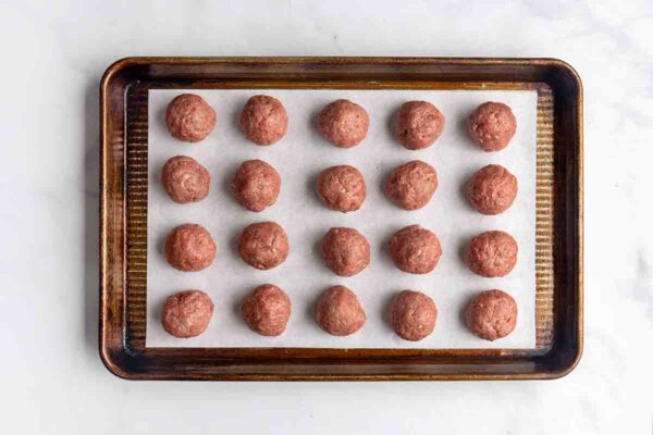 Twenty golf ball-sized meatballs on a parchment-lined baking sheet.