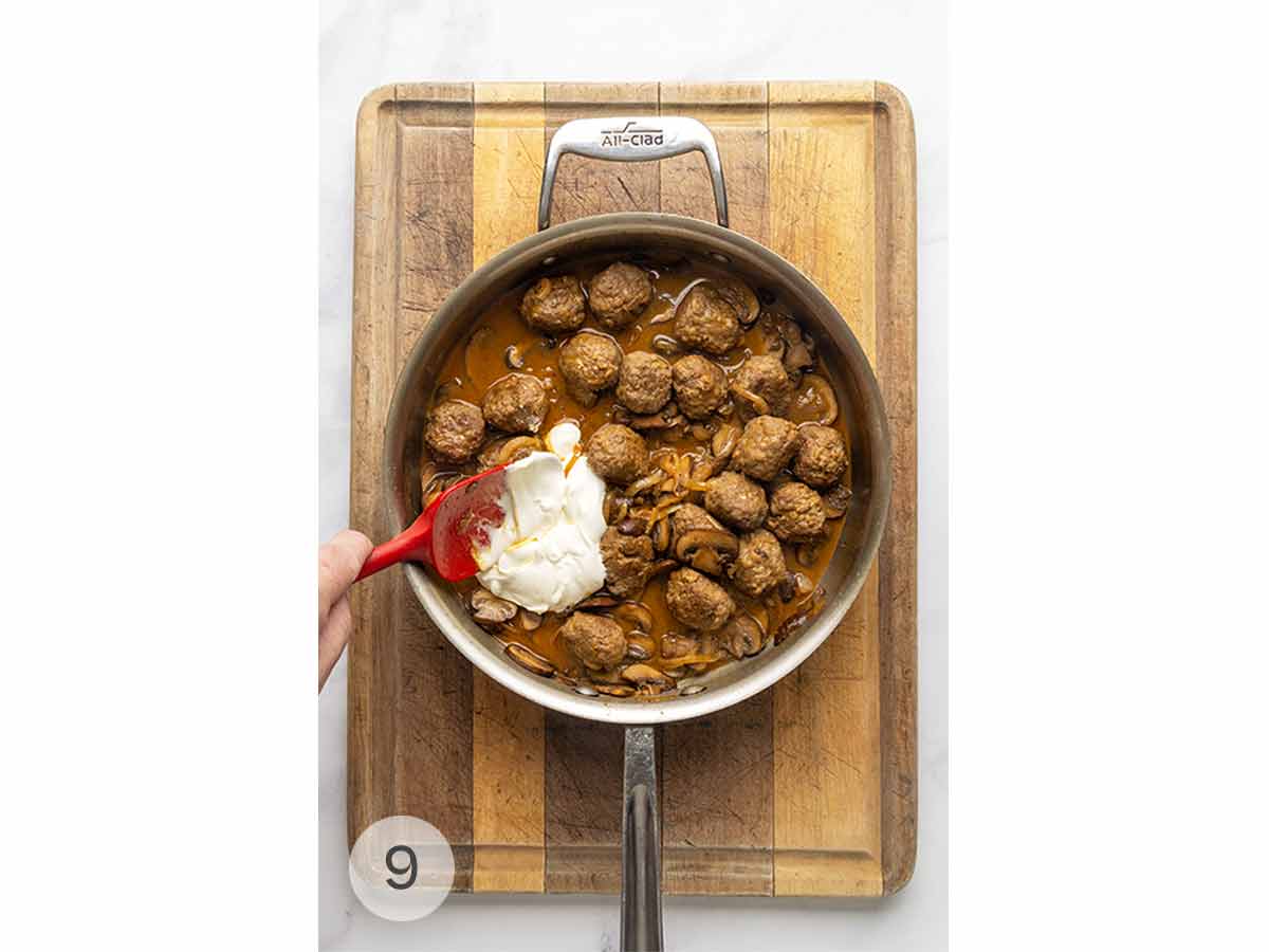 A skillet filled with meatball Stroganoff and a spatula stirring in sour cream.