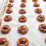 A parchment lined baking sheet filled with rows of round peanut butter cookies with chocolate centers.