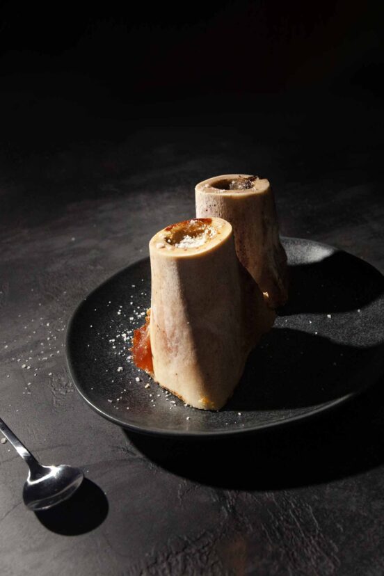 Two pieces of roasted bone marrow sprinkled with flaky salt on a black plate.