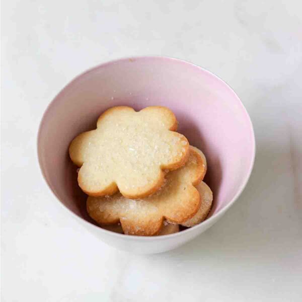A pink bowl filled with flower-shaped sugar cookies topped with decorating sugar.