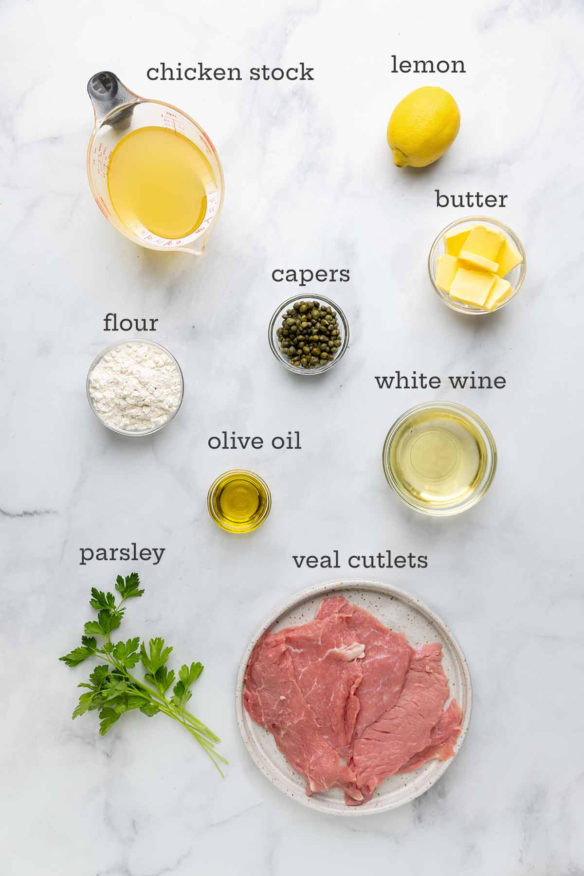 The ingredients for veal piccata--veal cutlets, lemon, flour, butter, olive oil, white wine, caper, and parsley