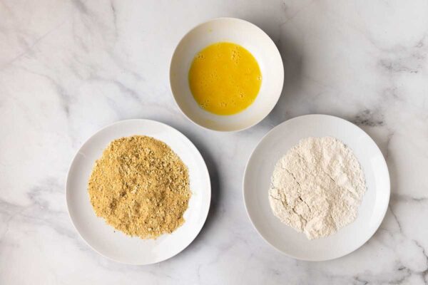 Bowls of flour, breadcrumbs, and beaten egg set up for a breading station.