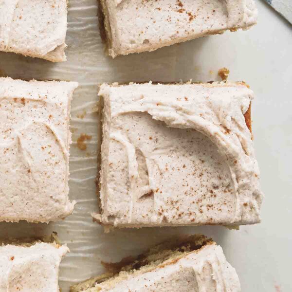 Brown butter snickerdoodle cake cut into six pieces on a piece of parchment paper, with a serving knife nearby.