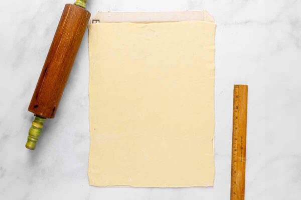 A rolled out sheet of puff pastry, a ruler, and a rolling pin.