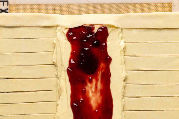 Strips of puff pastry being folded over a cheese and jam filling to make a Danish.