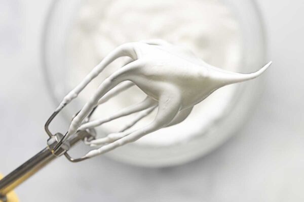 A closeup of a beater with whipped egg whites on it.