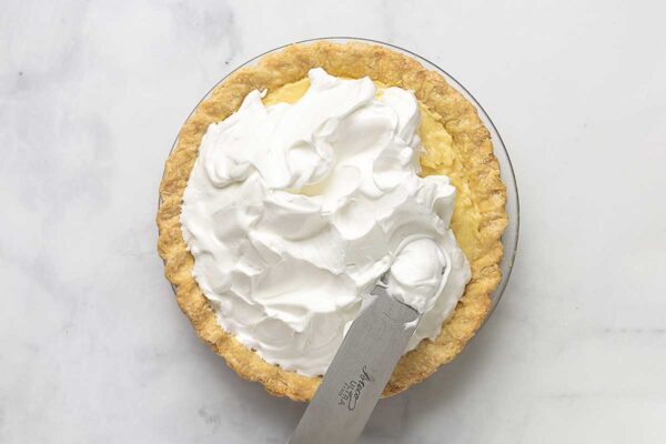 A coconut cream pie with meringue being slathered on it.